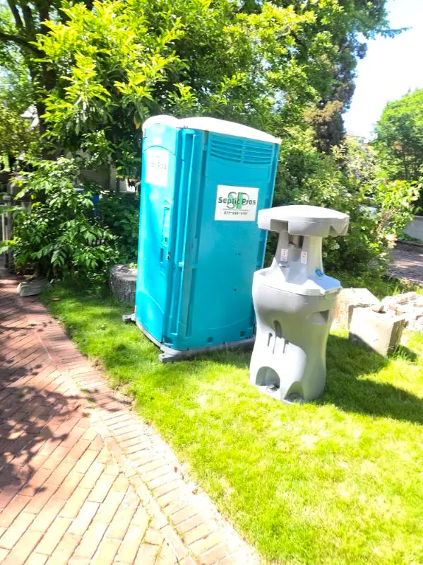 A clean Septic Pros portable toilet and handwashing station on a residential lawn