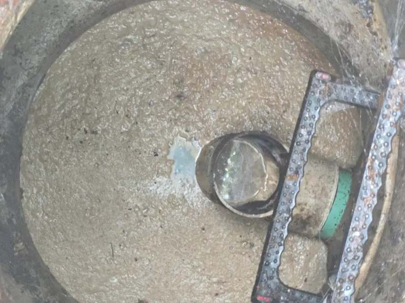 Checking the baffle and sludge level inside a pumped-down septic tank during an inspection